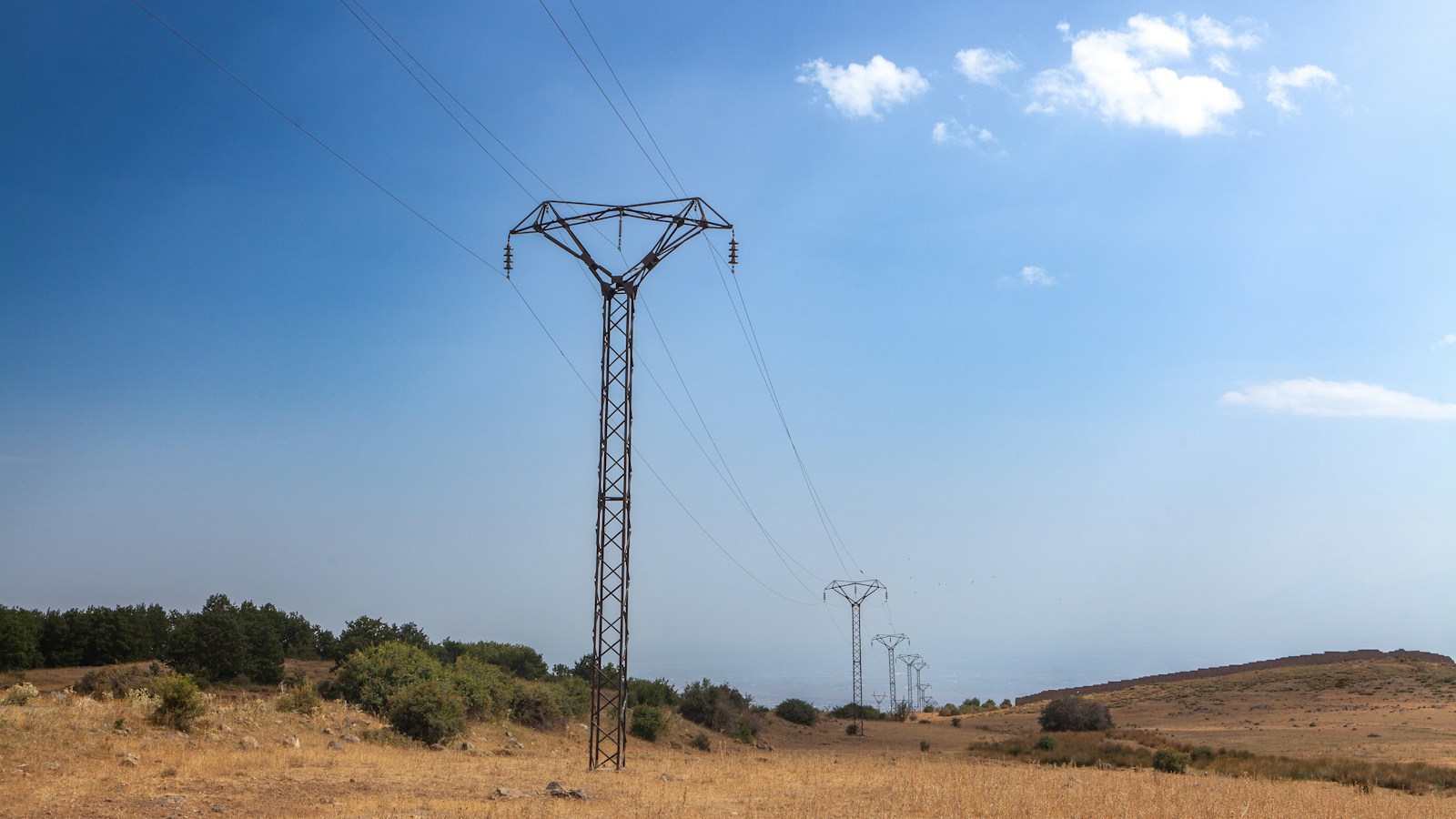 High-voltage transmission lines crossing a dry grassy landscape.